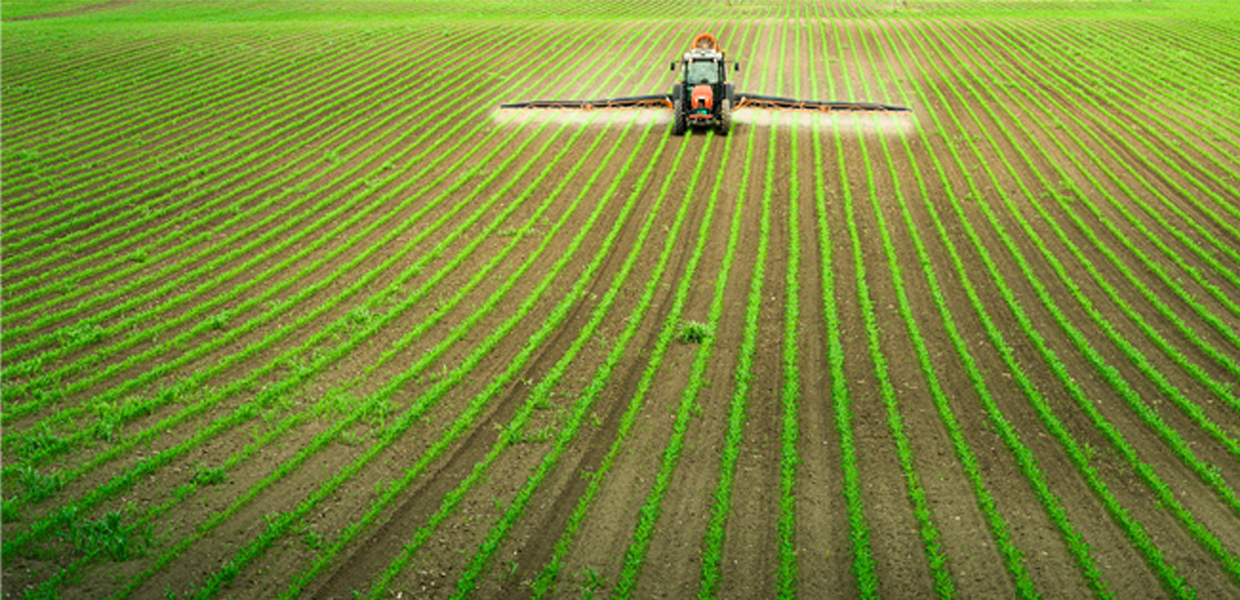 Tracteur pulvérisant un champ agricole, illustrant les solutions de BioService pour les odeurs agricoles.